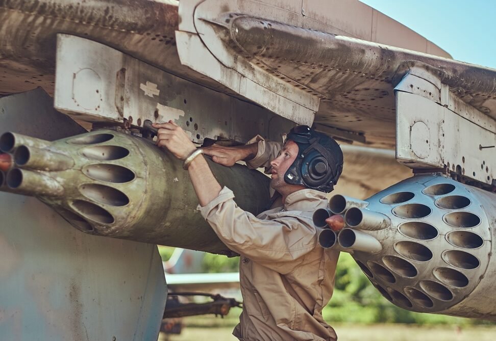 Mechanic in uniform and flying helmet repair old war fighter interceptor in an open-air museum.